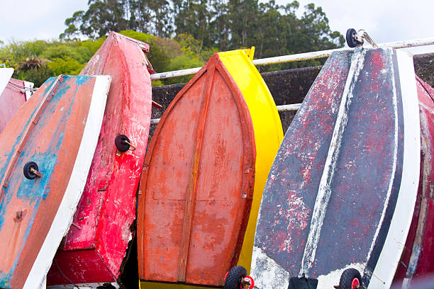 Multicolored fishing boats leaning over railing, drying upside down on harbor dock ,forest in the background. Lorbé, A Coruña province, Galicia, Spain.