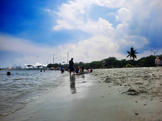 Ancol, North Jakarta, Indonesia - November 30, 2025 - Crowds Enjoying a Sunny Day at Ancol Beach in North Jakarta, a slight tweak on the sky to enhance the impression of a bright sunny day