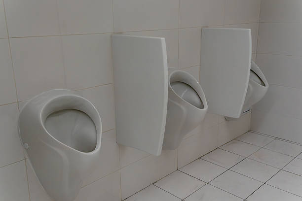 White ceramic urinal on tiled wall in public restroom. Minimalist restroom design with sleek urinal and sterile tiled surfaces in urban infrastructure.