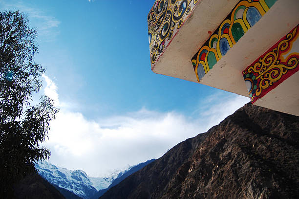 Colorful architectural structure with intricate decorations overlooks a mountainous landscape under a bright blue sky, showcasing natural beauty and cultural design.