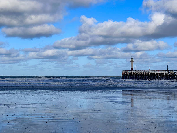 Nieuwpoort, West-Vlaanderen, Belgium, Ocotber 25th, 2025, Calm reflective beach with distant lighthouse, mirror-like wet sand and soft clouds creating tranquil coastal scene, serene light