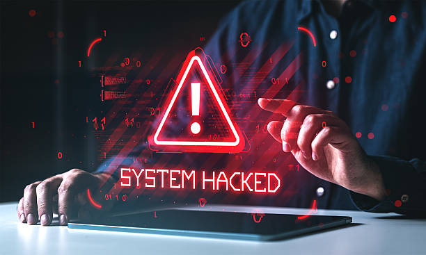 istock Cybersecurity warning with red alert triangle and system hacked message on digital screen in front of user touching tablet interface in dark room. 2251980798