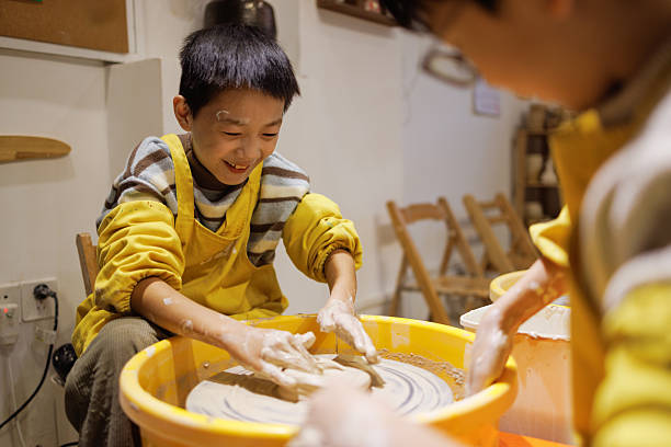 Smart boy pick clay while looking though hole at pottery workshop.Skilled diverse highschool student working and modeling dough while laugh at happy child at art lesson. Creative art. Edification.