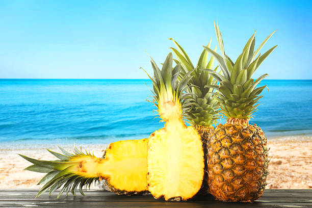 Fresh ripe pineapples on wooden table against seascape. Space for text