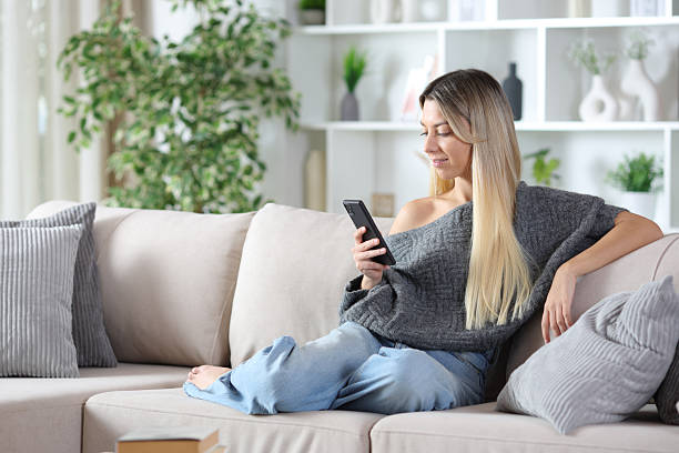 istock Blonde woman using cell phone sitting on a couch 2252000074