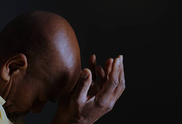 man praying to god with hands together portrait view of Caribbean man praying with black background with people stock photo stock image