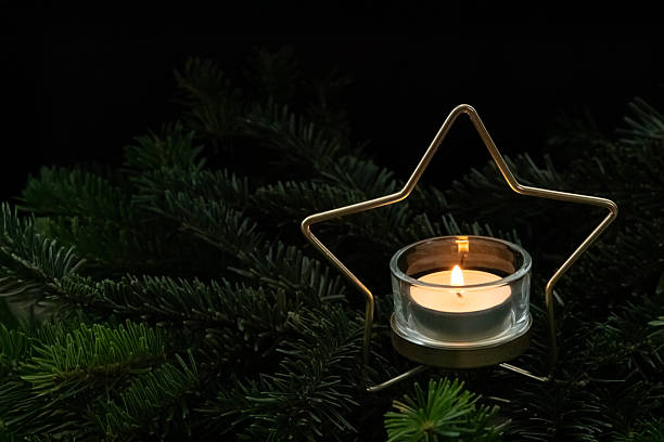 Lit candle placed inside a star shaped holder on a dark background, creating a warm and cozy Christmas atmosphere.