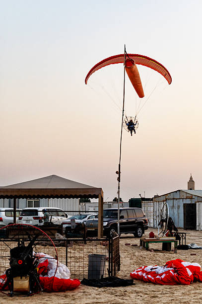 A paramotor pilot aproaching the airfield for landing at sunset. In the foreground a windsock.