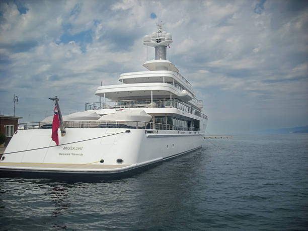 Aerial drone view of a luxury superyacht with a helipad, anchored in a calm turquoise bay at sunrise. A symbol of wealth, travel, and exclusive lifestyle in a beautiful mediterranean location