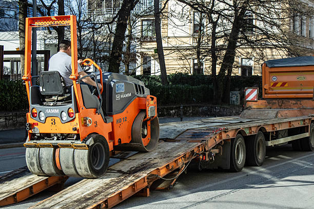 Ljubljana, Slovenia,  March 9, 2025, A worker secures an asphalt roller onto a flatbed truck in Ljubljana, Slovenia, on March 9, 2025, during road construction operations under clear daylight conditions.