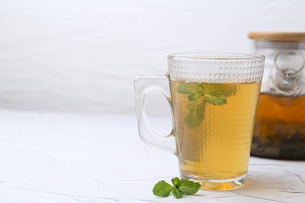 istock Aromatic mint tea and fresh leaves on white textured table, closeup. Space for text 2252008684