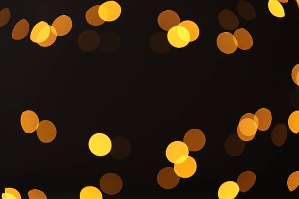 Blurred view of golden lights on black background, bokeh effect