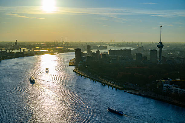 Euromast Rotterdam sunset skyline from a height view at the New Maas. In the far distance the port of Rotterdam is visible on the horizon. The Euromast on the right, standing at 185 meters  tall, it was originally built in 1960, designed by architect Huig Maaskant and engineer G. J. de Haan, and it remains one of the tallest structures in the city of Rotterdam.