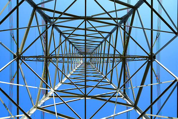High Voltage electricyty transmission towers with power lines an a blue sky and clouds in the background.