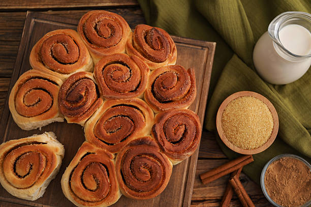 Freshly baked cinnamon rolls, milk and spices on wooden table, flat lay