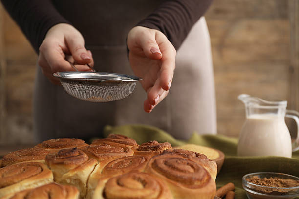 istock Woman with sieve adding cinnamon powder onto freshly baked rolls at table, closeup 2252013554