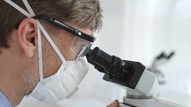 istock Male scientific researcher wearing protective gear examining sample through microscope, performing detailed laboratory investigation. Medicine and science concept 2252014427