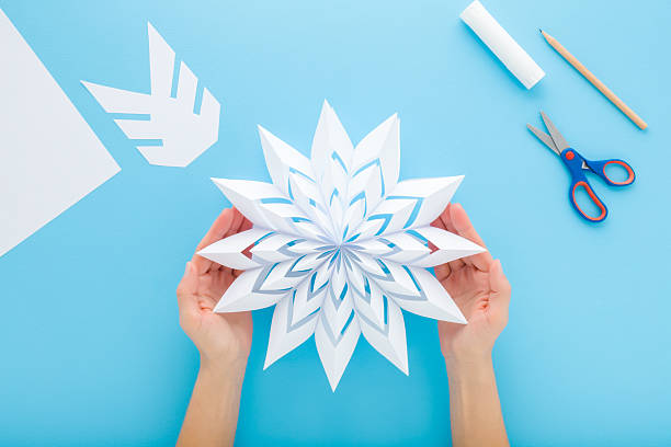 istock Woman hands holding and showing white snowflake shape from paper on light blue table background. Pastel color. Making decoration element for winter festive. Closeup. Point of view shot. Top down view. 2252020296