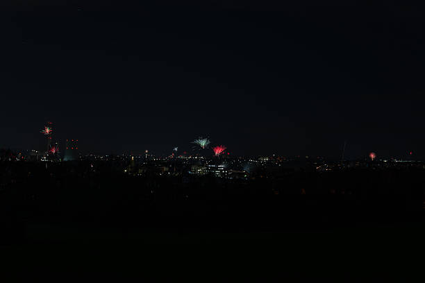 Wide view of scattered fireworks explosions over a distant, dark city skyline during a New Year's Eve celebration or festival, creating a subtle, festive atmosphere.