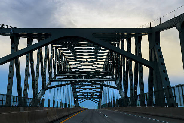 Large metal bridge connects two sides of road with cloudy sky overhead during early evening.