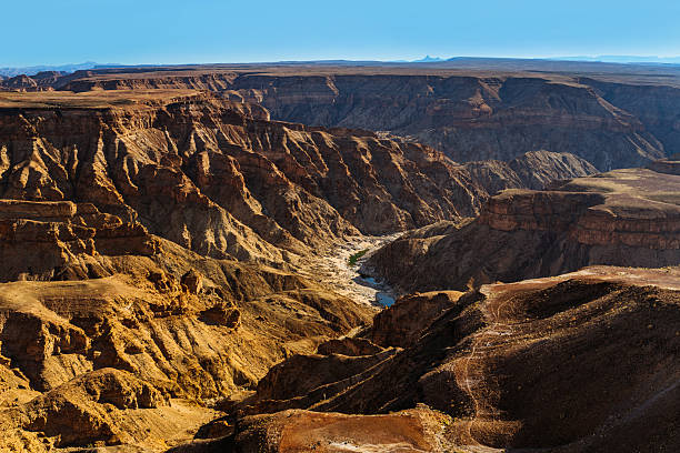 A sweeping view of Fish River Canyon in Namibia reveals rugged red rock formations, deep chasms, and a distant horizon under a clear blue sky, conveying vastness, solitude, and natural grandeur. Fish River Canyon in Namibia, the second largest canyon in the world and the largest in Africa.