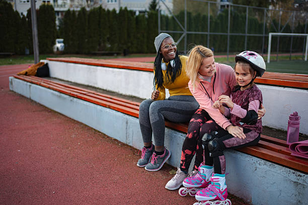 Two girls rollerblading on park path in spring, wearing helmets and knee pads. Children enjoy outdoor sport, combining fun and movement with healthy lifestyle, safety, joy, play and nature outdoors