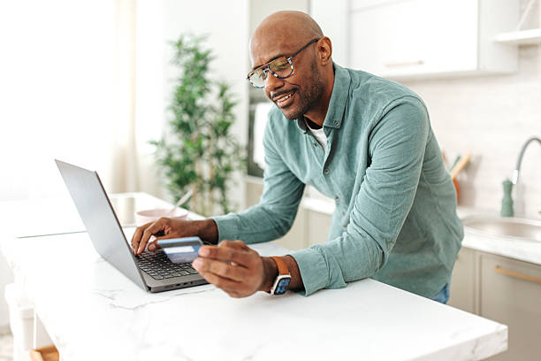 istock Man entering payment details on laptop in kitchen 2252032099