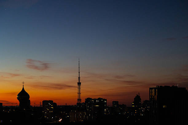 Kyiv Ukraine. Evening city skyline. Dark silhouette view. St Nicholas Cathedral dome. Pokrovsky Convent territory. Kyiv TV Tower background. Lukyanivka district. Sunset gradient sky. Orange twilight. Urban landscape. Orthodox architecture.