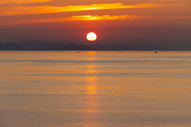 Sun setting over calm sea off the coast of Flores, Indonesia, with warm orange light reflecting across the smooth water surface.