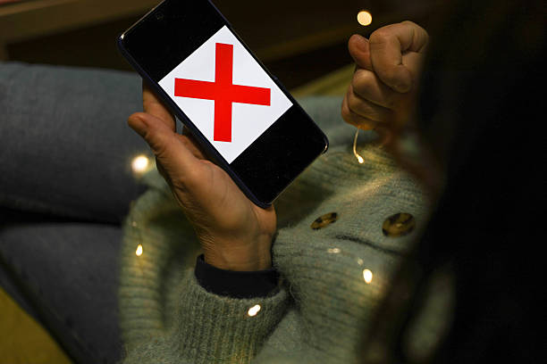 Close-Up Shot Of A Senior Woman Holding A Smartphone Displaying A Red Cross Symbol While Pointing At The Screen, Representing Error Message, Failed Action, Or Digital Warning In A Home Environment With Soft Decorative Lights.