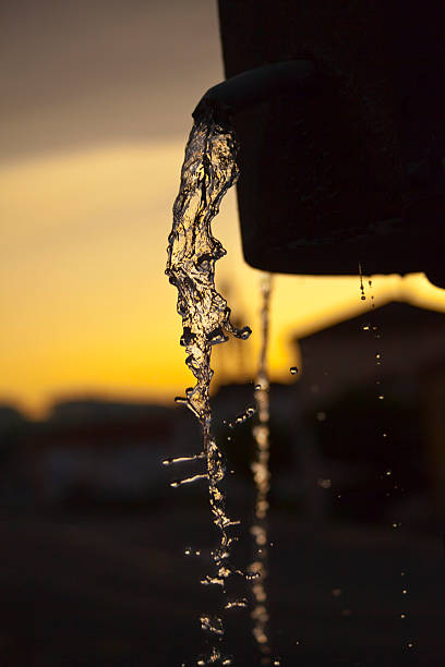 Water fountain, spurts and spouts at dusk ,  ancient stone Saleta drinking fountain seen along the Camino de Santiago ancient pilgrimage route, Boente church cattail in the background, A Coruña province, Galicia, Spain. Camino francés.