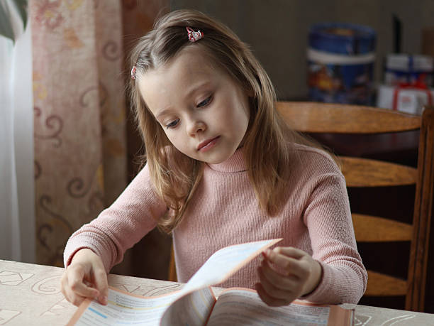 istock A girl is sitting at a table and leafing through a book. 2252047341