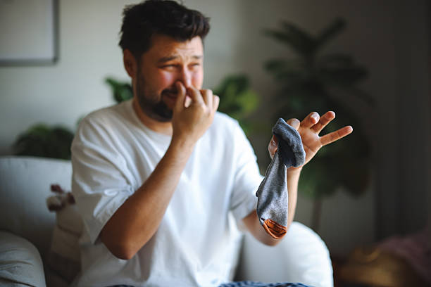 istock A man makes a disgusted face after sniffing a dirty sock while sitting on a couch in a casual setting 2252051791