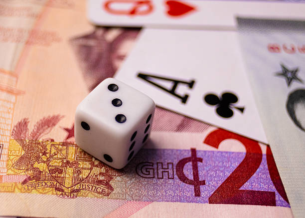 A white die showing 3, a playing card (Ace of Clubs), and currency (featuring the Ghanaian Cedi symbol) on a surface
