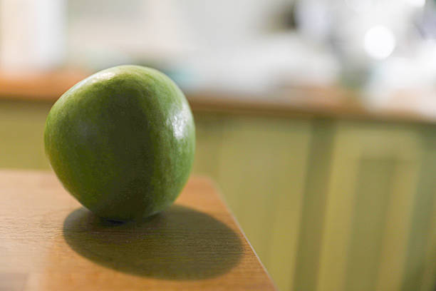 Green Apple Placed On A Wooden Kitchen Counter, Illuminated By Soft Indoor Light, Highlighting Its Fresh Texture And Natural Color, Symbolizing Healthy Eating And Fresh Produce.