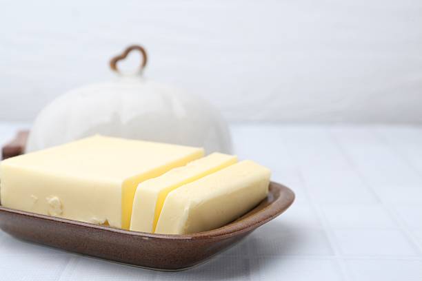 Cut tasty butter in dish on white tiled table, closeup. Space for text