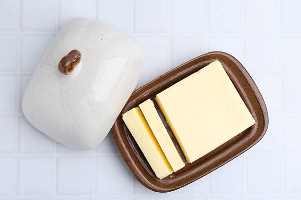 Cut tasty butter in dish on white tiled table, top view
