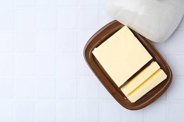 Cut tasty butter in dish on white tiled table, top view. Space for text