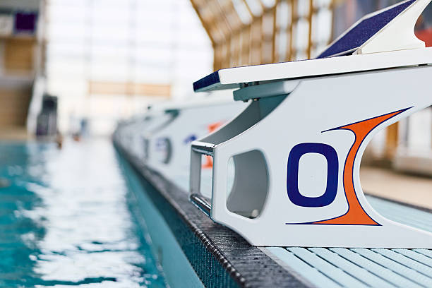 Swimming pool starting block positioned at the edge of an indoor pool, featuring crisp blue lighting, reflecting the clear water, ready for a race or competition