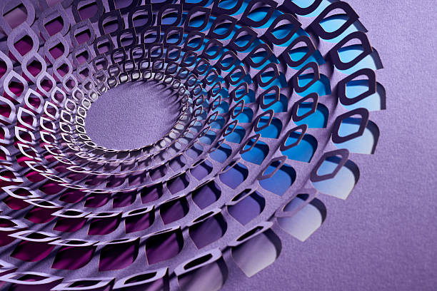 Still life photography of an abstract cut paper artwork arranged in a circular spiral. Layered geometric shapes in purple and blue tones create depth, motion, and rhythm, highlighting contemporary paper art, texture, and minimalist studio composition.
