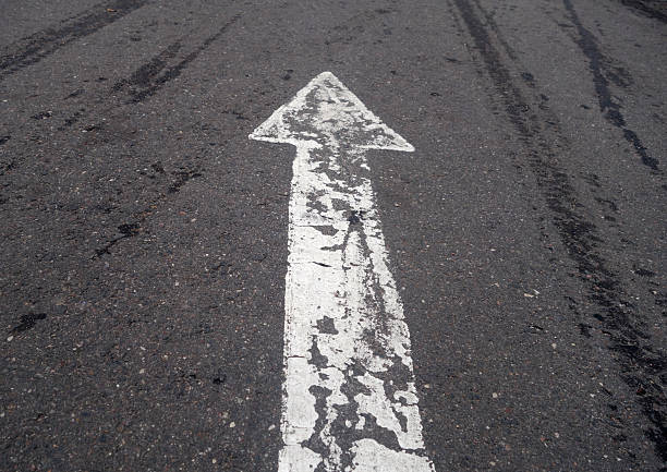 istock white painted pointing arrow on asphalt road with wet tyres tracks. 2252060088