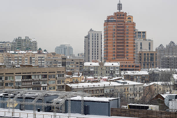 Winter city skyline with red brick skyscraper. Snow covers rooftops and HVAC equipment in Kyiv business district area.