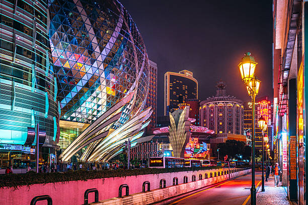 Vibrant Macau at night featuring futuristic glass buildings, neon signage, street lamps, and pedestrians along a lively city avenue. A striking urban landscape blending modern architecture with nightlife energy and travel appeal.