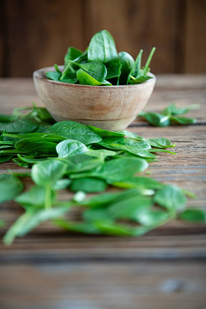 Fresh green spinach leaves in a wooden bowl placed on a rustic wooden table. Healthy organic leafy vegetables concept, clean eating, vegetarian and vegan food background. Top view and close-up compositions with copy space.