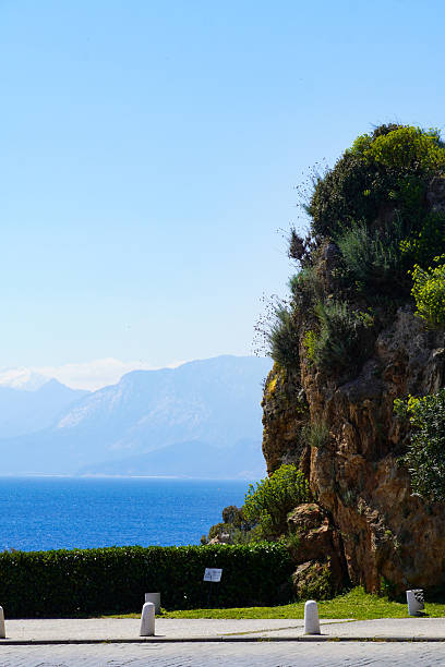 Elevated view of a coastal road stretching alongside Konyaalti Beach in Antalya, Turkey, with greenery, streetlights, and the Mediterranean Sea in the background