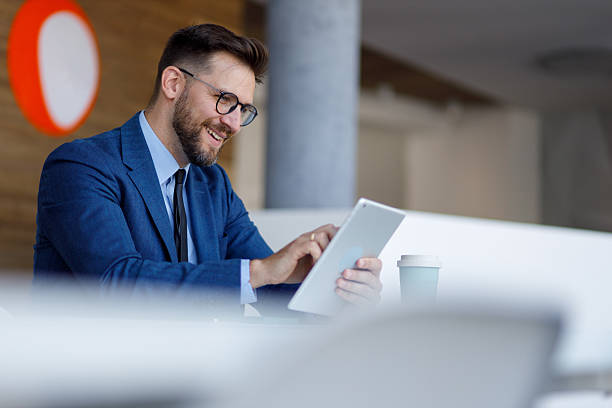 istock Businessman using digital tablet in modern office with coffee cup, smiling and working remotely 2252082334