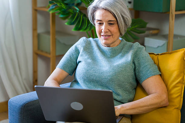 istock Senior woman relaxing on couch, using laptop at home 2252096313