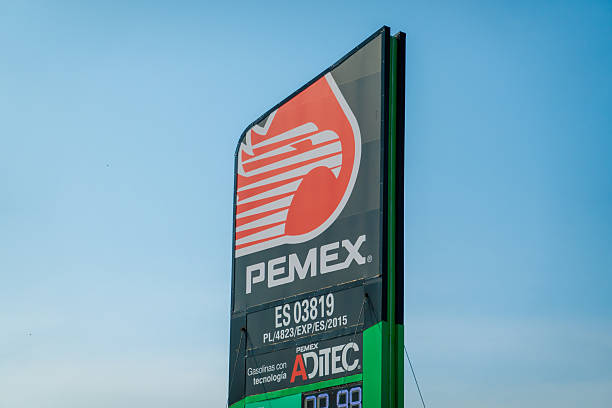 Huatulco, Oaxaca, Mexico. Dec 15, 2025. A tall, vertical PEMEX gasoline station sign featuring the national eagle logo and ADITEC branding against a clear blue sky on a sunny day.