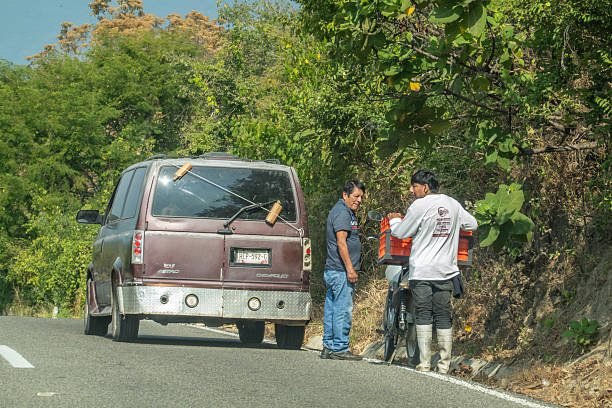 Huatulco, Oaxaca, Mexico. Dec 17, 2025. A low-angle shot of a modified Chevrolet Astro van with Mexican plates stopped by a green forest as two men stand by a motorcycle.