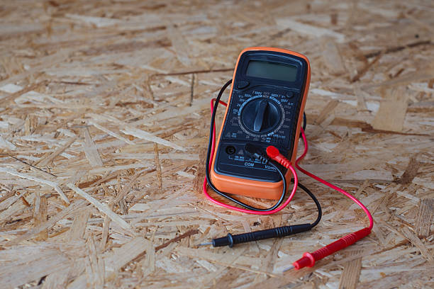 istock Orange and black digital multimeter with red and black test leads placed on oriented strand board OSB construction material. 2252097547